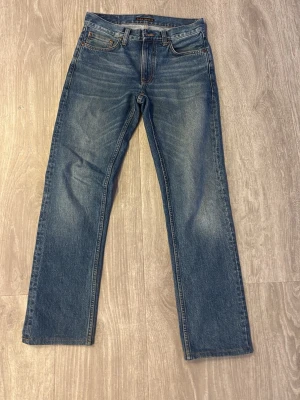 Gritty Jackson Nudie Jeans - Säljer ett par klassiska blå jeans från Nudie Jeans med rak passform och fem fickor. Jeansen har snygga slitningar framtill och bakfickor med Nudie Jeans signatursöm. Tillverkade i denim av bomull. Använda fåtal gånger, kom med frågor och prisförslag, jeansen är storlek 28/32 men är omgjorda till va 28/30 men kan även passa 28/31
