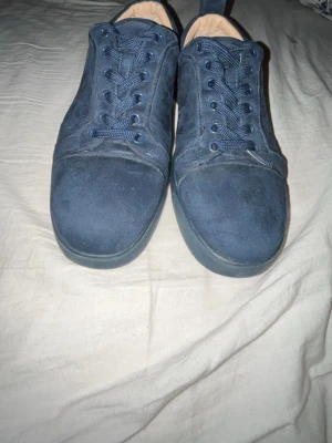 Blåa sneakers från Christian Louboutin - Snygga blåa sneakers från Christian Louboutin i mocka med klassisk röd sula och matchande blå skosnören. Låg modell med rund tå och diskret design som sticker ut med den ikoniska röda undersidan. Perfekta för dig som gillar exklusiva detaljer.