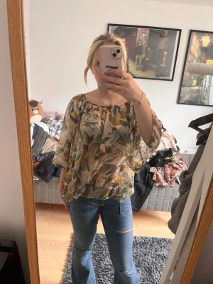 Blommig transparent blus med vida ärmar - Säljer en luftig blus med blommigt mönster i beige, grönt och brunt. Blusen är transparent, har rundad halsringning och vida trekvartsärmar. Perfekt för dig som gillar en avslappnad och bohemisk stil.