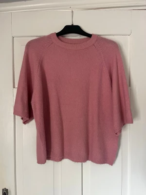 Rosa stickad tröja från 157 - Mysig rosa stickad tröja från 157 med rund halsringning och halvlånga ärmar. Tröjan har en enkel, avslappnad passform och ribbade detaljer vid halsen, ärmslut och nederkant. Perfekt för lager på lager och en chill look. Stor i storleken. 