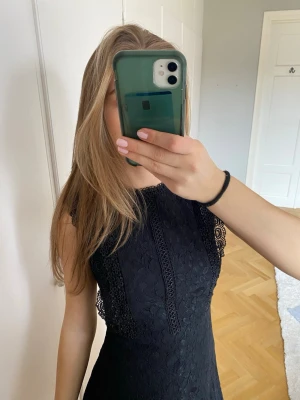 Ärmlös svart spetsklänning  - Säljer en svart, ärmlös kortklänning med spetsdetaljer och figurnära passform. Klänningen har rund halsringning och dragkedja baktill.