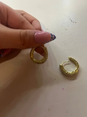 Guldpläterade creoler med mönster - Säljer ett par chunky guldpläterade creoler med snyggt ingraverat mönster. Örhängena har en rundad form och är perfekta för dig som gillar statement-smycken. 