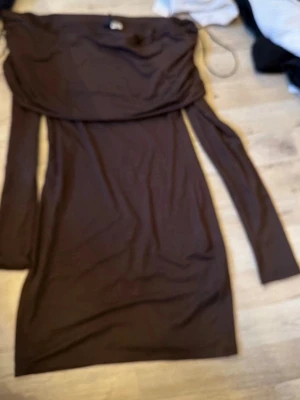 Brun offshoulder klänning - Snygg brun klänning med offshoulder-design och långa ärmar. Klänningen har en kroppsnära passform och är tillverkad i ett mjukt, stretchigt material som ger en bekväm känsla. Perfekt för dig som vill ha en enkel men stilren look.