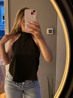 Svart halterneck topp med knyt - Säljer en svart halterneck topp med knyt i nacken. Toppen är ärmlös och har en croppad passform som passar perfekt till höga jeans eller kjol. 