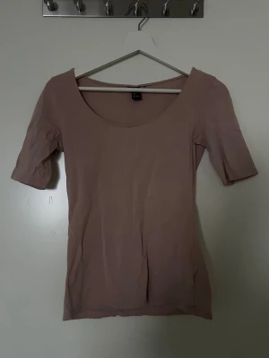 Beige/rosa topp  - En enkel och stilren beige/rosa topp med rund halsringning och halvlånga ärmar. Figurnära passform och mjukt material som känns bekvämt mot huden. 