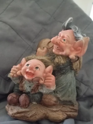 Trollfigur i polyresin med detaljer - Säljer en dekorativ trollfigur i polyresin med två troll som sitter tillsammans. Figurerna har stora öron, buskigt hår och ringar i öronen. Kläderna är målade i jordnära färger som grått, grönt och brunt. Perfekt som prydnad eller samlarobjekt.