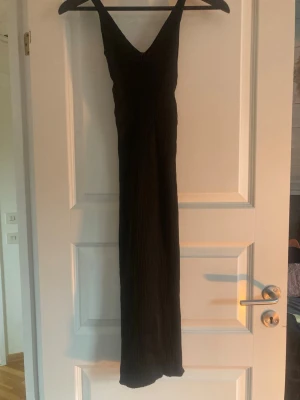 Svart ribbad långklänning - Snygg svart långklänning med v-ringning och breda axelband. Klänningen är ribbad och har en kroppsnära passform som framhäver siluetten. Perfekt för dig som gillar en stilren och enkel look.
