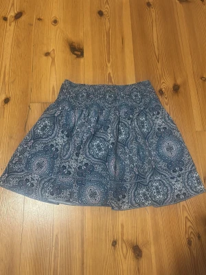 Blå kjol från SHEIN - Kort kjol från SHEIN med blått paisleymönster och resår i midjan. Kjolen har en luftig passform och är perfekt för varma dagar. Tillverkad i ett lätt och bekvämt material som känns skönt mot huden. Säljer då den inte kommer till användning längre💙