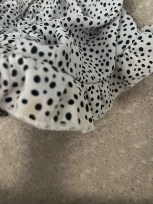 Prickig vit blus med puffärmar - Supersöt vit blus med svarta prickar och puffiga korta ärmar. Smockad överdel och volangkant nedtill ger en trendig och feminin look. Perfekt för dig som gillar detaljer och vill sticka ut lite extra. En liten gul flack på magen som ej går bort.