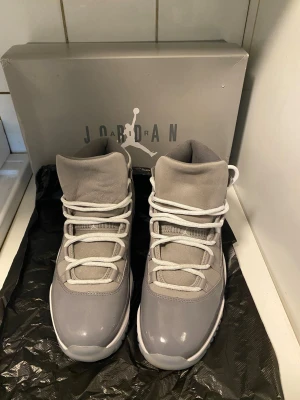 Air Jordan 11 Cool Grey  - Snygga Air Jordan 11 Cool Grey sneakers med högt skaft. Skorna har en grå ovandel i mocka och lackat läder, vita skosnören och en genomskinlig sula med grå detaljer. Ikonisk Jumpman-logga på sidan och klassisk retrostil som sticker ut. Skorna funkar både som basket skor men även som ett dagligt val. Låda inkluderas såklart. För mer frågor är det bara att höra av sig i dm 