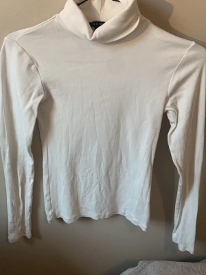 Vit polotröja från Amisu - Säljer en enkel och stilren vit polotröja från Amisu i storlek XS. Tröjan har lång ärm och hög polokrage, perfekt att matcha med jeans eller kjol. Tillverkad i mjukt och stretchigt material för en bekväm passform.