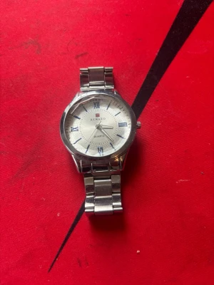 Silverfärgad Reward armbandsklocka - Stilren armbandsklocka från Reward med silverfärgat metallarmband och vit urtavla. Klockan har romerska siffror i blått och klassisk rund form. Perfekt accessoar för dig som gillar en tidlös look.