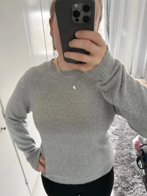 Ljusgrå stickad tröja - Mysig ljusgrå stickad tröja med rund halsringning och ribbade muddar vid ärmslut och nederkant. Tröjan har en klassisk passform och håller dig varm under kyliga dagar.