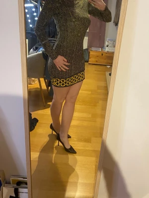 Svart och gul mönstrad kortklänning - Snygg svart kortklänning med gula fyrkantiga prickar och ett grafiskt mönster i gult och svart längst ner. Klänningen har lång ärm och figurnära passform, perfekt för dig som gillar att sticka ut. Materialet känns stretchigt och bekvämt.