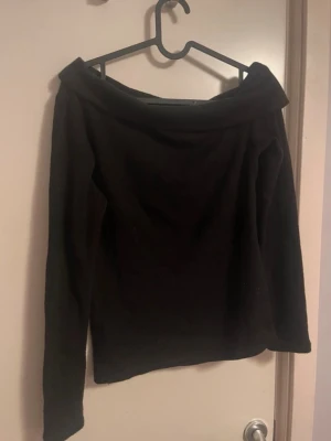 Svart offshoulder topp - Stilren svart offshoulder topp med långa ärmar och bred krage. Perfekt för dig som vill ha en enkel men snygg topp till din garderob. Mjuk och bekväm, passar till många olika looks.