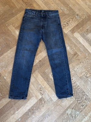 Svarta/Mörkgråa raka jeans - Säljer ett par mörka jeans med rak passform och klassisk femficksdesign i storlek W27/L30. Jeansen har en lätt tvättad look och normal midja. Materialet är denim i bomull. Perfekta för en avslappnad och stilren vardagsoutfit.