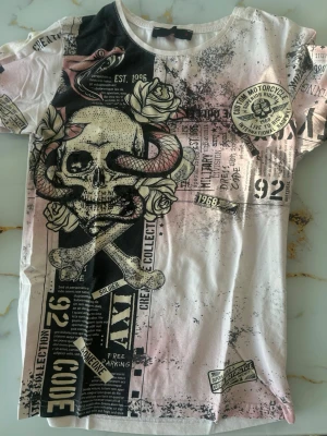 T-shirt med dödskalle och ormmotiv - Unik t-shirt från Cipo & Baxx med stort tryck av dödskalle, ormar och rosor i svart, vitt och beige. Coola detaljer med text och grafiska element över hela tröjan. Rund halsringning och korta ärmar. Perfekt för dig som gillar edgy streetstyle.