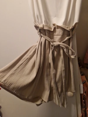 Byxdress - Supersnygg beige byxdress med breda ben. Dragkedja på ena sidan. Dressen har ett knytband i midjan. 