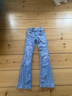 Ljusblå utsvängda jeans medelhög midja - Säljer ett par ljusblå jeans med utsvängda ben och jeansen har medel/hög midja. Väldigt stretchiga och långa i benen. Har en liten liten grå prick vid låret på höger sida och är även lite missfärgade längst nere vid benen. 