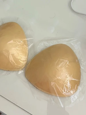 Beige bh-inlägg i skum - Säljer ett par beige bh-inlägg i skum som ger extra form och stöd. Perfekta att lägga i din bh för en naturlig push-up-effekt. Inläggen är trekantiga och tunna, och kommer i ett mjukt material som känns bekvämt mot huden.