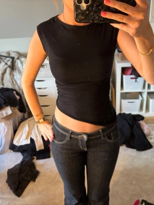 Svart tight ärmlös topp - Säljer en svart, tight och croppad topp med ärmlös design. Toppen har en enkel och stilren look med rund halsringning och smickrande passform. Perfekt att matcha med jeans eller kjol för en trendig outfit.