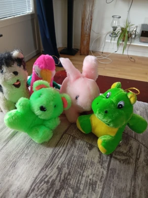 Fem mjukisdjur i olika färger - Säljer ett gäng mjukisdjur: en grön nalle, en grön och gul groda, en rosa kanin, en rosa papegoja och en svartvit hund. Alla är små och gjorda i mjukt plyschmaterial, perfekta som dekoration eller leksaker.