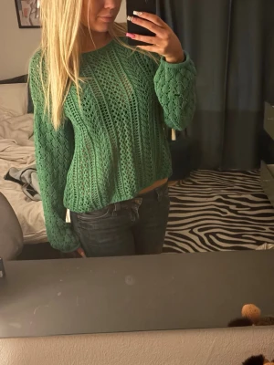 Grön stickad tröja med hålmönster  - Snygg grön stickad tröja med hålmönster och rund hals. Tröjan har långa ärmar och en avslappnad passform. Perfekt att styla med jeans för en trendig look. Materialet är mjukt och luftigt💗