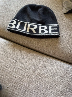Svart mössa från Burberry - Snygg svart mössa från Burberry med vit logotyptext runt kanten. Tillverkad i mjukt stickat material som känns skönt mot huden. Perfekt accessoar för att hålla värmen och samtidigt se trendig ut.