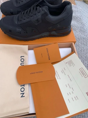 Svarta Louis Vuitton sneakers - Snygga helsvarta Louis Vuitton sneakers med monogramdetaljer på sidan och tåpartiet. Skorna har en låg silhuett, klassisk snörning och är tillverkade i en mix av läder och textil. Perfekta för dig som vill ha en exklusiv och stilren look.