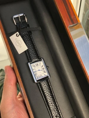 Svensk märke. elegant klocka + äkta läderband - Stilren NY med etikett klocka från cosmos med fyrkantig silverfärgad boett och svart läderarmband med struktur. Urtavlan är vit med romerska siffror och blå visare. Perfekt accessoar för dig som gillar klassisk och tidlös design. Snabb leverans