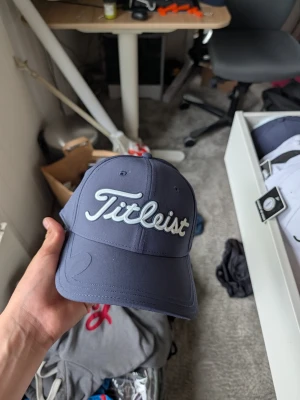 Mörkblå Titleist keps - Snygg mörkblå keps från Titleist med broderad logga framtill i vitt. Klassisk böjd skärm och justerbar passform baktill. Tillverkad i ett lätt och ventilerande material som passar perfekt för golf eller vardagsstil.