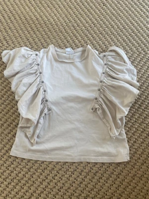 Vit topp med volangärmar från Zara - Supersöt vit/creme topp från Zara med stora volangärmar och dekorativa knappar längs axlarna. Tillverkad i mjuk bomull, perfekt för dig som vill sticka ut lite extra. Enkel att matcha till olika outfits!💞💞