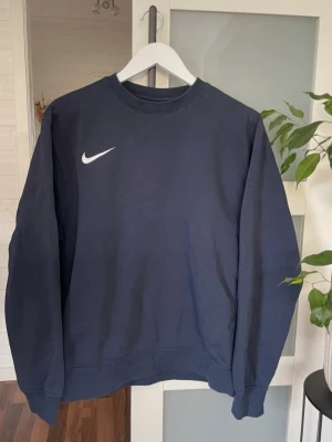 Mörkblå crewneck från Nike  - Mörkblå sweatshirt från Nike i klassisk crewneck-modell. Tröjan har rund halsringning, långa ärmar och diskret Nike-logga framtill. Tillverkad i mjukt material som känns skönt mot huden. Perfekt för en avslappnad och sportig stil.