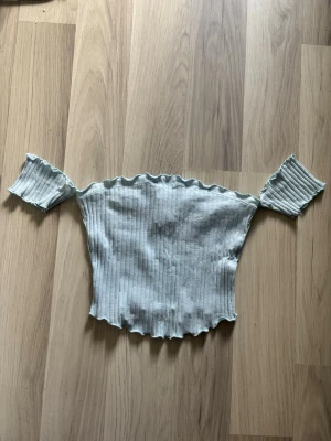 Off shoulder topp - Superfin ljusblå offshoulder topp från New Yorker  i ribbat material. Toppen har korta ärmar och vågig kant både upptill och nedtill, vilket ger en söt och trendig look. Perfekt till sommaren.