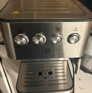 Espressomaskin  - Snygg espressomaskin i borstat rostfritt stål med fyra vridreglage på framsidan och avtagbar droppbricka. Maskinen har en modern, stilren design och vattenbehållare på sidan. Perfekt för dig som vill göra kaffe hemma.