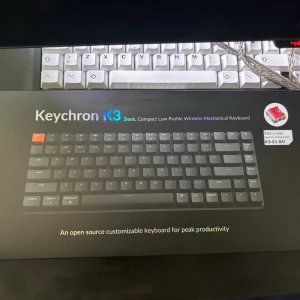 Keychron K3 trådlöst mekaniskt tangentbord - Keychron K3 är ett slimmat och kompakt trådlöst mekaniskt tangentbord med låg profil och RGB-belysning. Tangentbordet har svart bas med grå och orange tangenter, och stödjer upp till tre enheter samtidigt. Perfekt för dig som vill ha ett snyggt och anpassningsbart tangentbord.