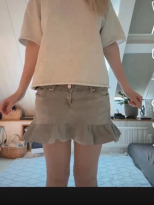 Grå  volangkjol med jeanslook - Egen syd kjol. Midjemåttet är 40cm💕💕💕Snygg beige kortkjol med volangkant och klassisk jeanslook. Kjolen har fickor fram och bak samt knapp och dragkedja i midjan. Perfekt för dig som gillar en avslappnad men trendig stil.