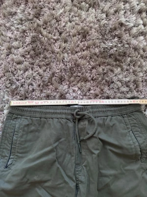 Olivgröna shorts från Reserved - Säljer ett par olivgröna shorts från Reserved i storlek L. De har snörning i midjan och två sidofickor. Materialet är mjukt och känns som bomull, perfekt för varma dagar. Enkel och stilren design som funkar till många olika outfits.