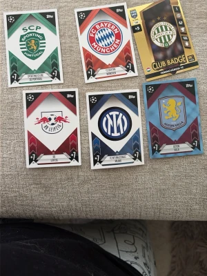 Fotbollskort med klubbmärken - Säljer sex stycken fotbollskort från Topps med klubbmärken från Sporting CP, FC Bayern München, Ferencváros TC, RB Leipzig, Inter och Aston Villa. Korten har olika färger och klubbarnas logotyper i centrum. Perfekt för samlare eller fotbollsintresserade.