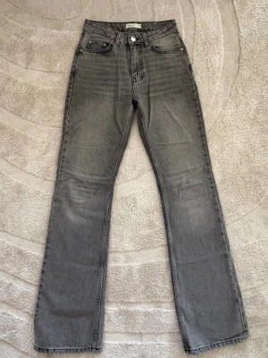 Grå raka jeans från Gina Tricot - Snygga grå jeans från Gina Tricot med raka ben och klassisk femficksdesign. Jeansen har hög midja och är tillverkade i ett mjukt denimtyg. Perfekta för en avslappnad och trendig look.
