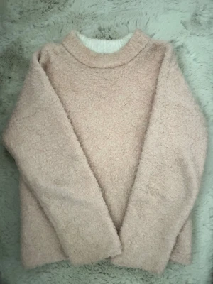 Ljusrosa stickad tröja River Island - Mysig ljusrosa stickad tröja från River Island Studios i relaxed fit. Tröjan har en fluffig, mjuk textur och rund halsringning. Perfekt för att hålla sig varm och snygg under kyliga dagar.