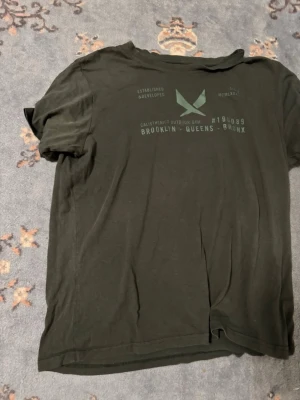 Svart t-shirt med tryck Brooklyn - Svart t-shirt med tryck på bröstet där det står Brooklyn, Queens och Bronx. T-shirten har rund halsringning och korta ärmar. Materialet ser ut att vara bomull eller bomullsblandning. Perfekt för en avslappnad streetwear-look.