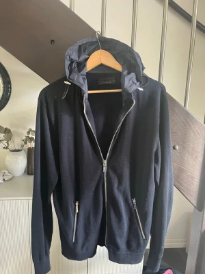 Fet cardigan  - fet cardigan  med dragkedja framtill och två fickor med dragkedja. Huva i ett glansigt material med dragsko. Perfekt för en avslappnad och stilren look. Står size L sitter som M
