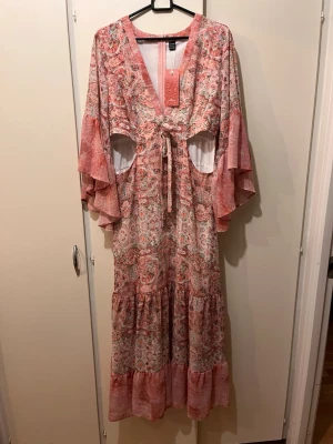 Ny rosa lång boho klänning strl L  - Helt ny rosa mönstrig klänning cut open strl L. Alla lappar kvar. Jättebra kvalitet i tyget. Jag är 160 cm lång för referens. 