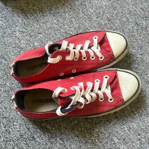 Röda låga Converse sneakers - Klassiska röda Converse sneakers i lågt snitt med vit gummisula och tå, vita skosnören och metallöljetter. Ovandelen är i röd canvas och insidan är svart. Perfekta för en avslappnad och cool stil.