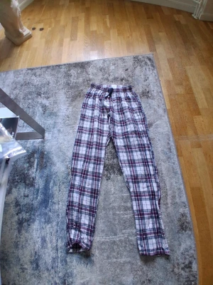 Rutiga pyjamasbyxor Time to Lounge - Mysiga pyjamasbyxor från Time to Lounge i röd, blå och vit rutig bomull. Byxorna har resår i midjan och dragsko för extra komfort. Perfekta för chillkvällar hemma eller när du bara vill ta det lugnt.