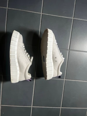 Beige chunky sneakers från Eytys - Säljer ett par beige chunky sneakers från Eytys med grov sula och vita skosnören. Skorna har canvasmaterial och tydliga sömmar, samt logga på plösen. Perfekta för dig som gillar en clean men edgy stil.