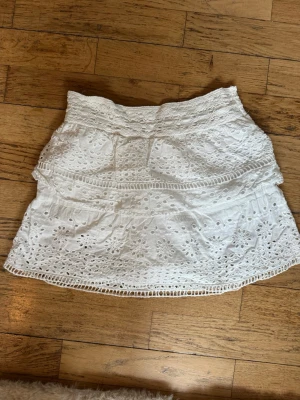 Vit broderad kortkjol med volang - Söt vit kortkjol med broderade blommor och volangdetaljer. Kjolen har bred resår i midjan😊