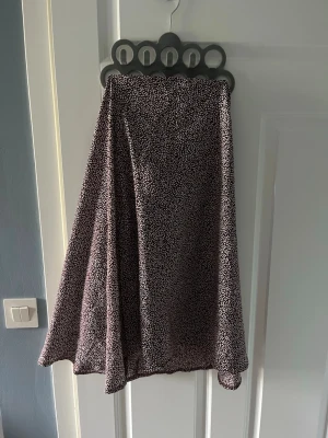 Brunvit prickig långkjol - Snygg bruntvit kjol med småprickigt mönster. Kjolen har en lätt utsvängd form och faller fint. Perfekt för dig som gillar en stilren men ändå lekfull look. Materialet känns mjukt och följsamt mot huden.