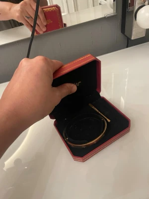 Guldfärgat stelt armband i ask - Snyggt stelt armband i guldfärg med gravyrdetaljer runt om. Armbandet har en elegant och minimalistisk design och kommer i en röd lyxig ask. Perfekt accessoar för att lyfta din stil och matcha med andra smycken.